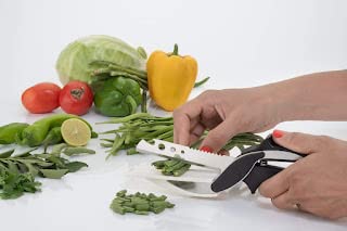 Hands cutting green beans with stainless steel and black multi functional kitchen scissors among fresh vegetables
