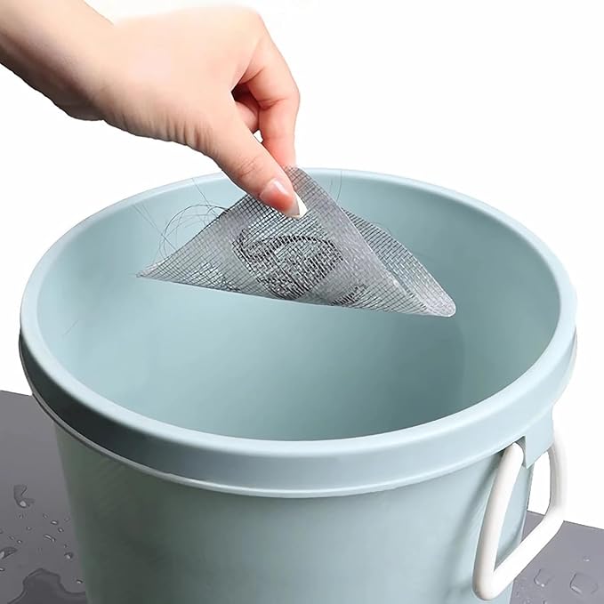 Hand holding shower mesh drain catcher stickers with trapped hair over a light blue bucket