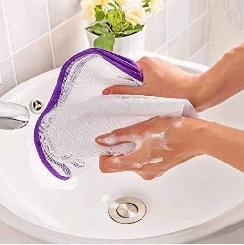 Hands cleaning an iron safety mesh pad over a bathroom sink with soap suds